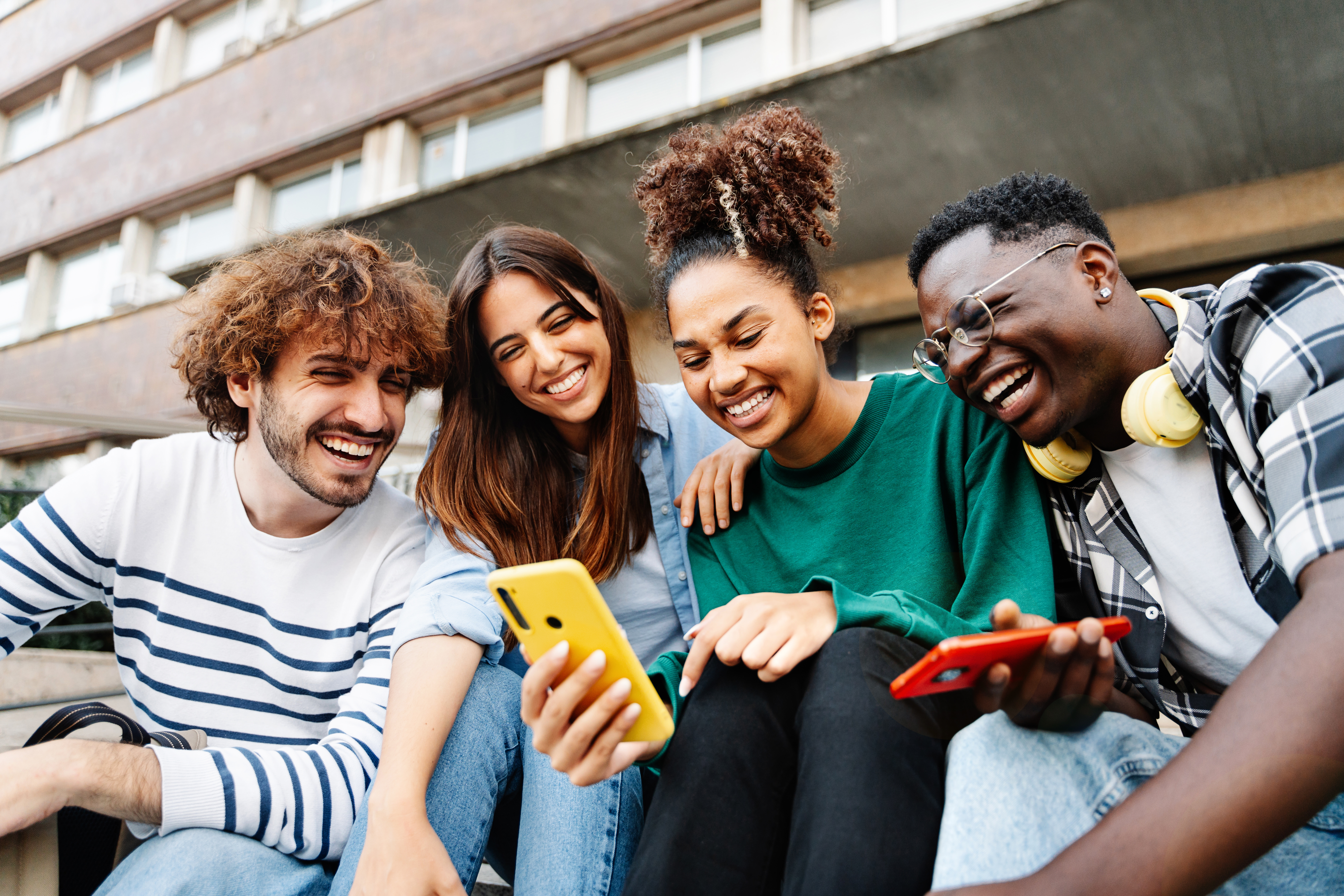 Group of university student friends sitting together using mobile phones to share content on social media Group of university student friends sitting together using mobile phones to share content on social media