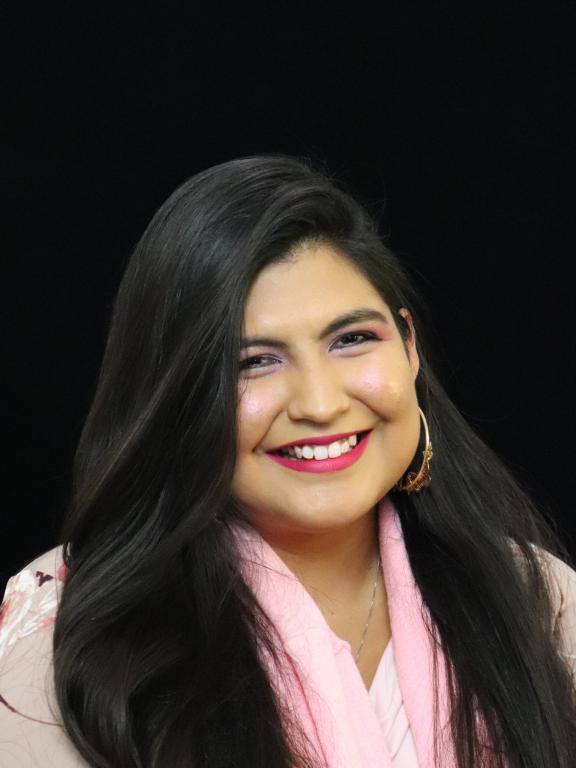 Professional headshot of a smiling woman with long dark hair, wearing a light pink scarf, in front of a black background.