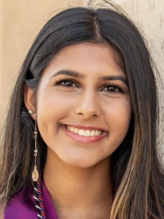 A close-up portrait of a smiling woman with long dark hair, wearing a long decorative earring.