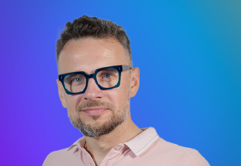 A person wearing a light pink collared shirt against a gradient blue and purple background.