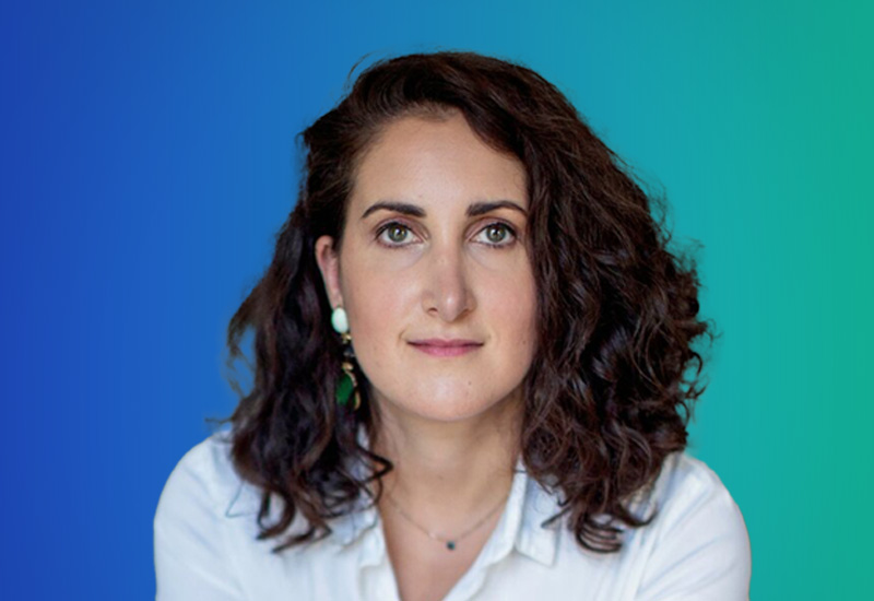 Portrait of a woman with curly dark hair, wearing a white shirt, in front of a blue and green gradient background.