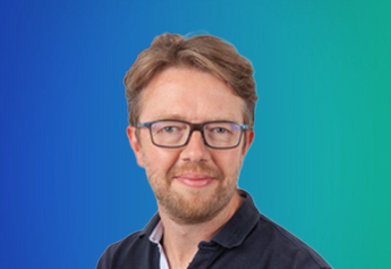 Professional headshot of a man with glasses and light brown hair, wearing a dark shirt, on a blue-green gradient background.