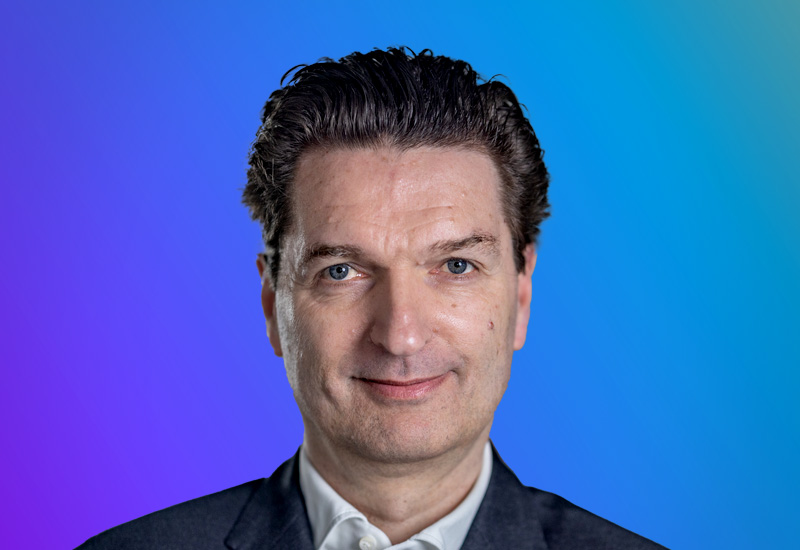 Professional headshot of a person in business attire on a blue and purple gradient background, used for AWS Summit Hamburg approved event materials.