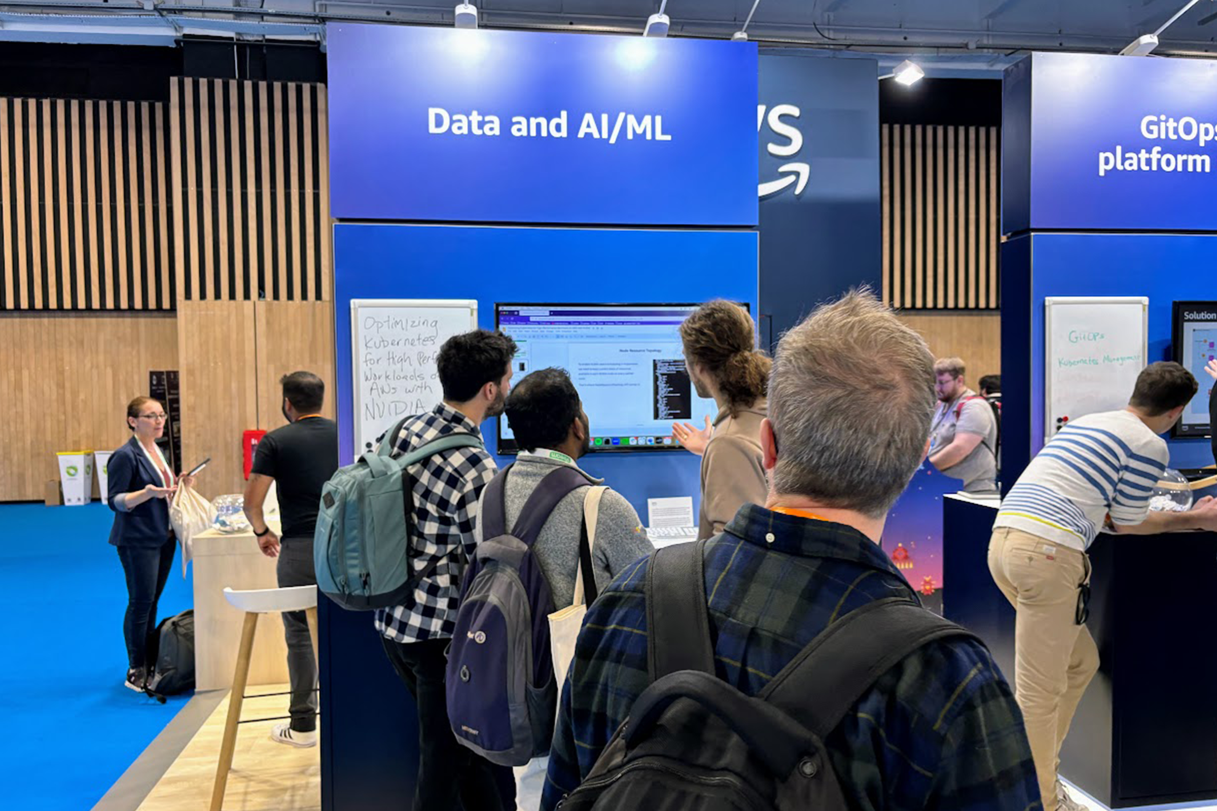 Attendees gather at the AWS booth during KubeCon to view a Data and AI/ML demonstration showcasing Kubernetes optimizations for high performance workloads, with displays and discussions about AI/ML solutions.
