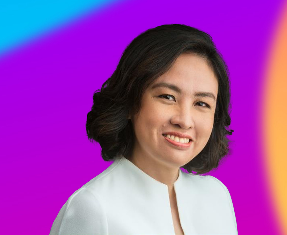 A person with shoulder-length dark hair wearing a white top, set against a vibrant gradient background of purple, blue, and orange.