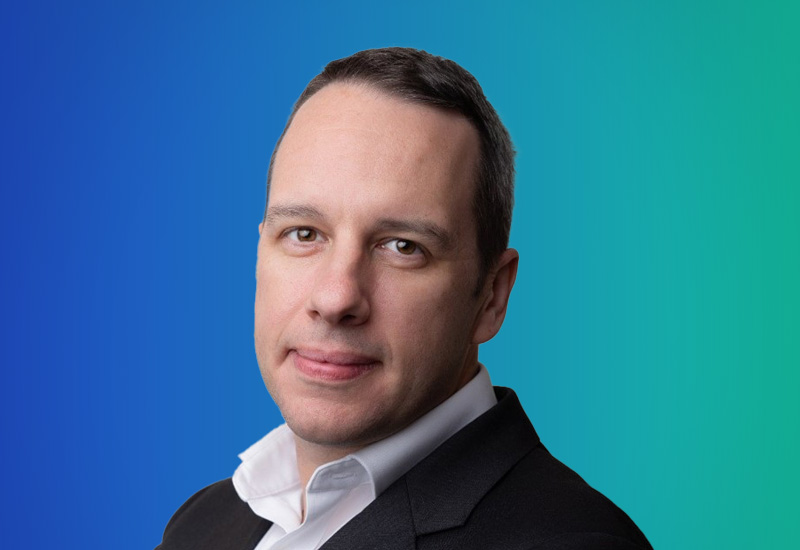 Professional headshot of a man in business attire with a blue-green gradient background.