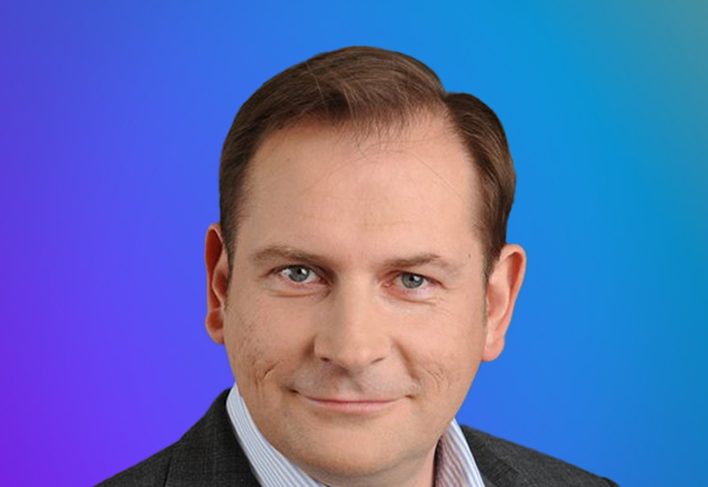 A person wearing a suit against a gradient blue and purple background.