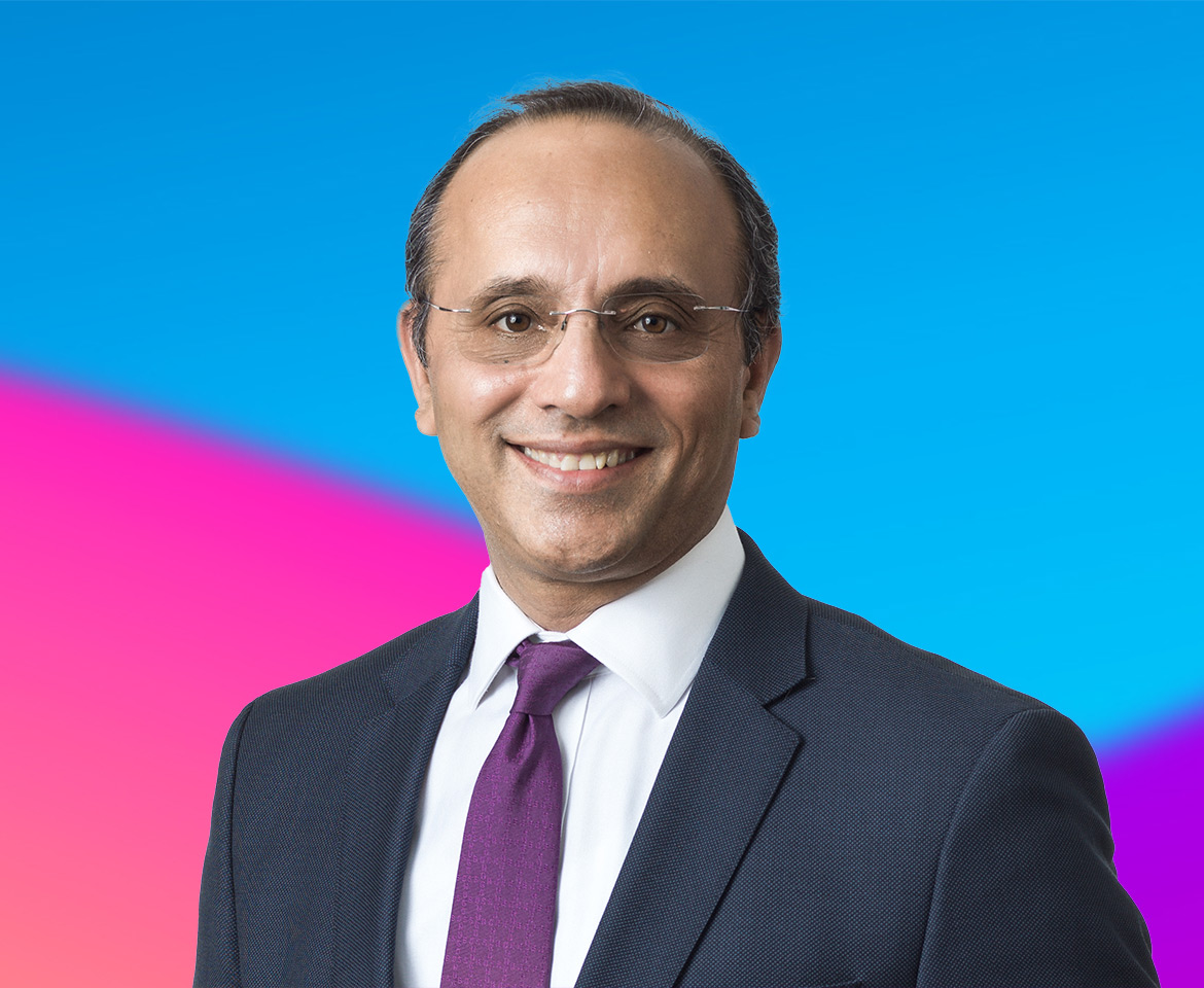 A person wearing a dark suit, white shirt, and purple tie against a vibrant blue and pink gradient background.