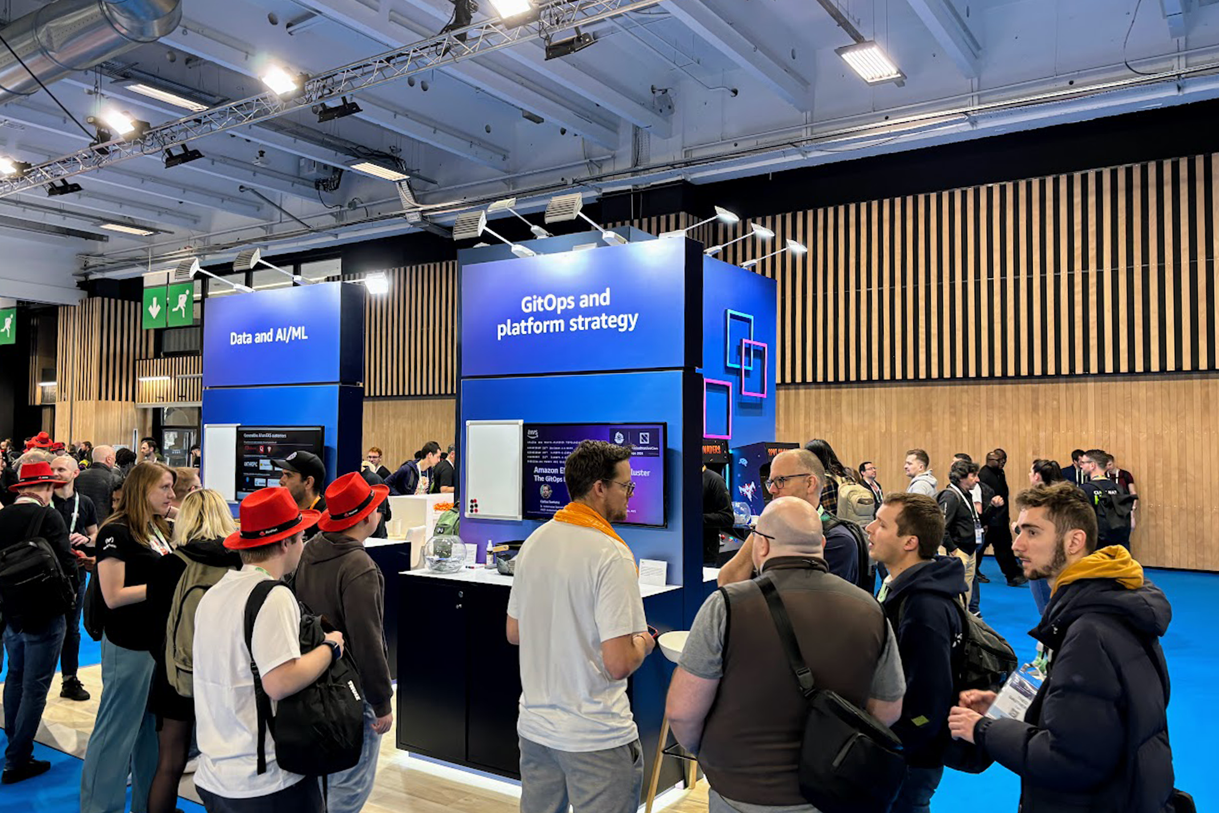 Attendees interacting at the AWS Retail booth during KubeCon, featuring sections on Data and AI/ML, and GitOps and platform strategy.