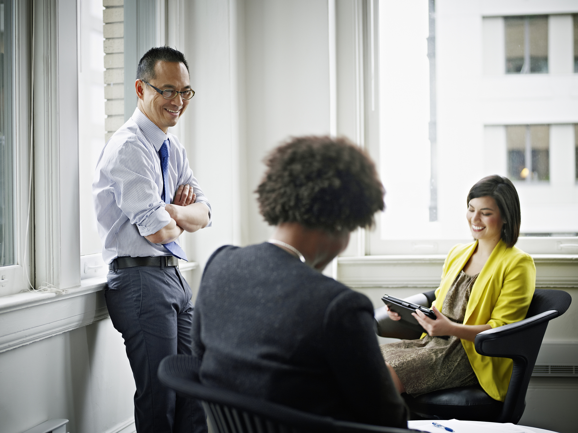 Three coworkers in discussion in office conference room smiling and laughing