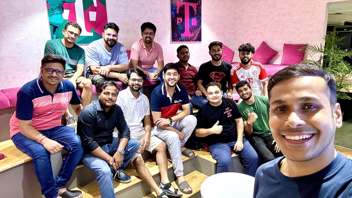 A group of people sitting and posing in a brightly lit room with pink cushions and T-Mobile-themed wall art.