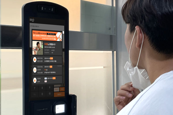 A person wearing a face mask uses a BROJ facial recognition access terminal at a secure entry point.