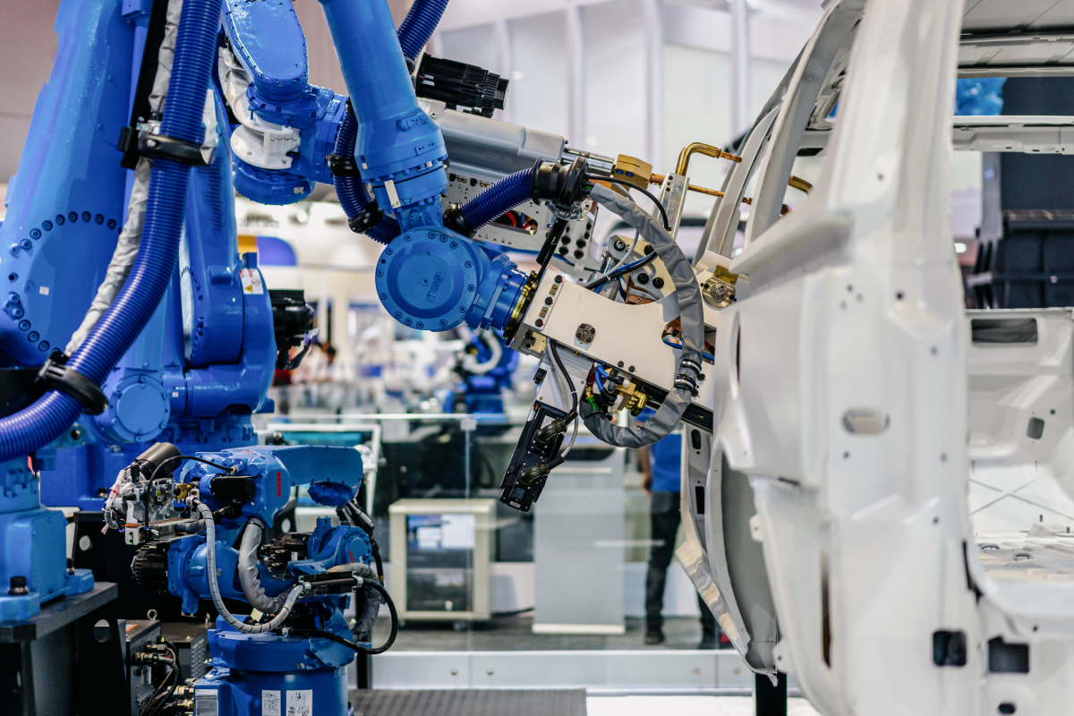 A blue industrial robot arm works on assembling or welding the chassis of a white automobile in a modern automated automotive manufacturing facility.