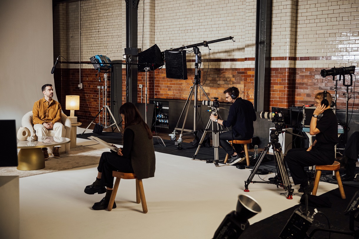 A behind-the-scenes look at the filming of an interview set for AWS Pioneers featuring Rayan Chikhi. The setup includes professional cameras, lighting equipment, a director, and technical crew in a studio environment.