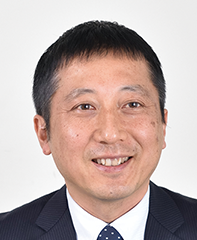 Portrait of a smiling businessman in a suit and tie, photographed against a plain background. The photo is formatted for use in a business or professional context.