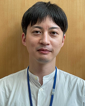A man wearing a white shirt and blue lanyard poses for a portrait in front of a wooden background.