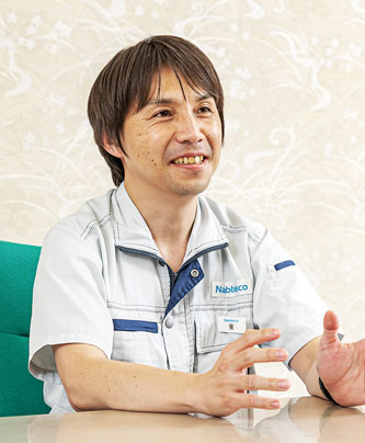 A person wearing a Nabtesco uniform gesturing with their hands while seated at a table.