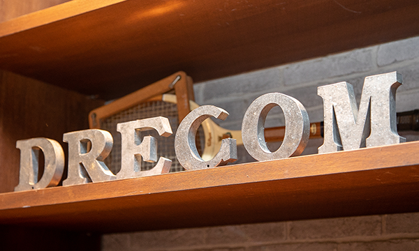 Metal letters spelling 'DRECOM' displayed on a wooden shelf, as seen in an AWS case study setting.