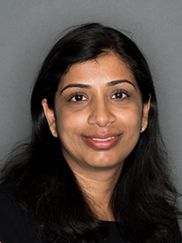 Professional headshot of a woman with long dark hair, wearing a black top, set against a plain grey background.