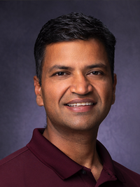 A professional headshot of Hemant Malik against a dark background. He is wearing a maroon collared shirt and is smiling at the camera.