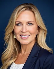 A professional business portrait of a smiling woman with long blonde hair, wearing a dark blazer against a blue background.